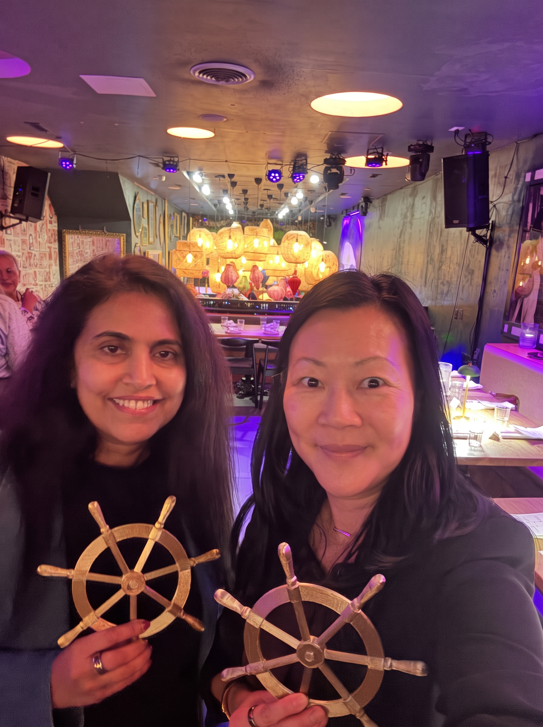 Two guests smiling at the camera while holding ship's wheel keepsakes at the Philadelphia gathering