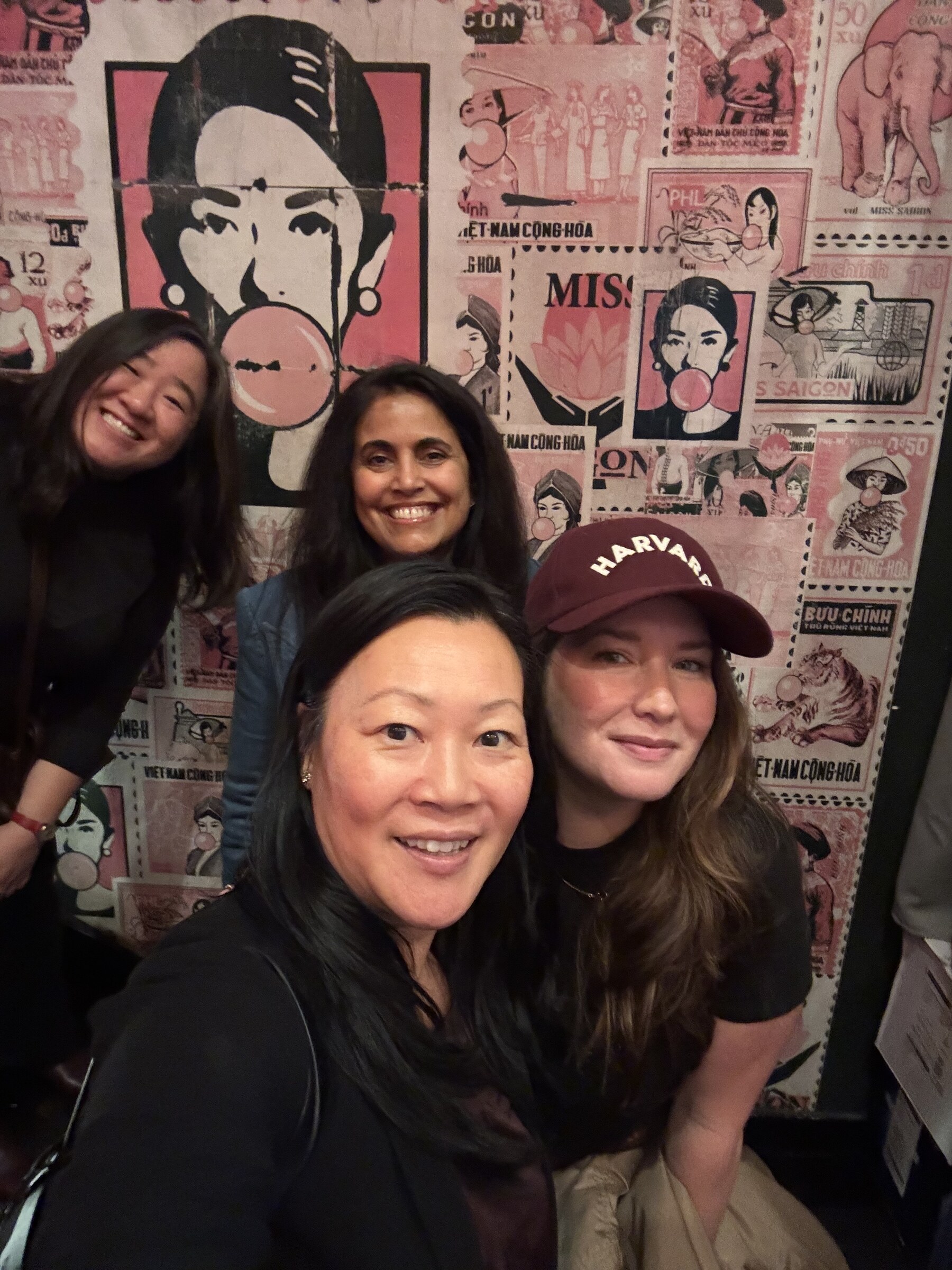 Four guests taking a selfie together in front of the vintage Vietnam poster wall at the Philadelphia gathering