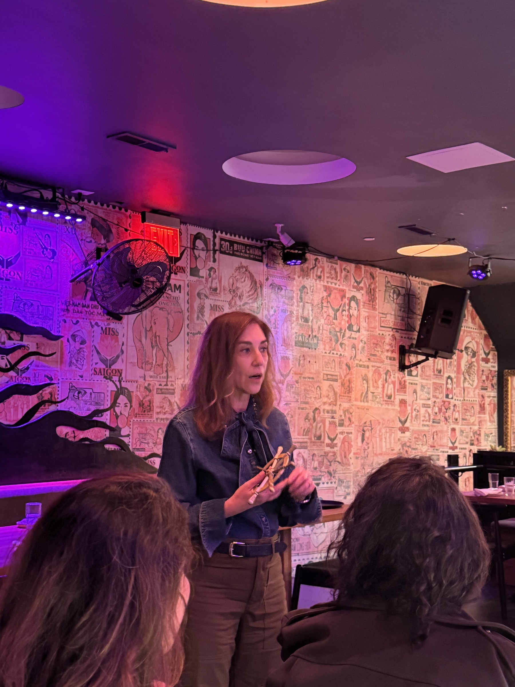 Guest speaker holding a wooden ship's wheel craft in front of a poster-covered wall